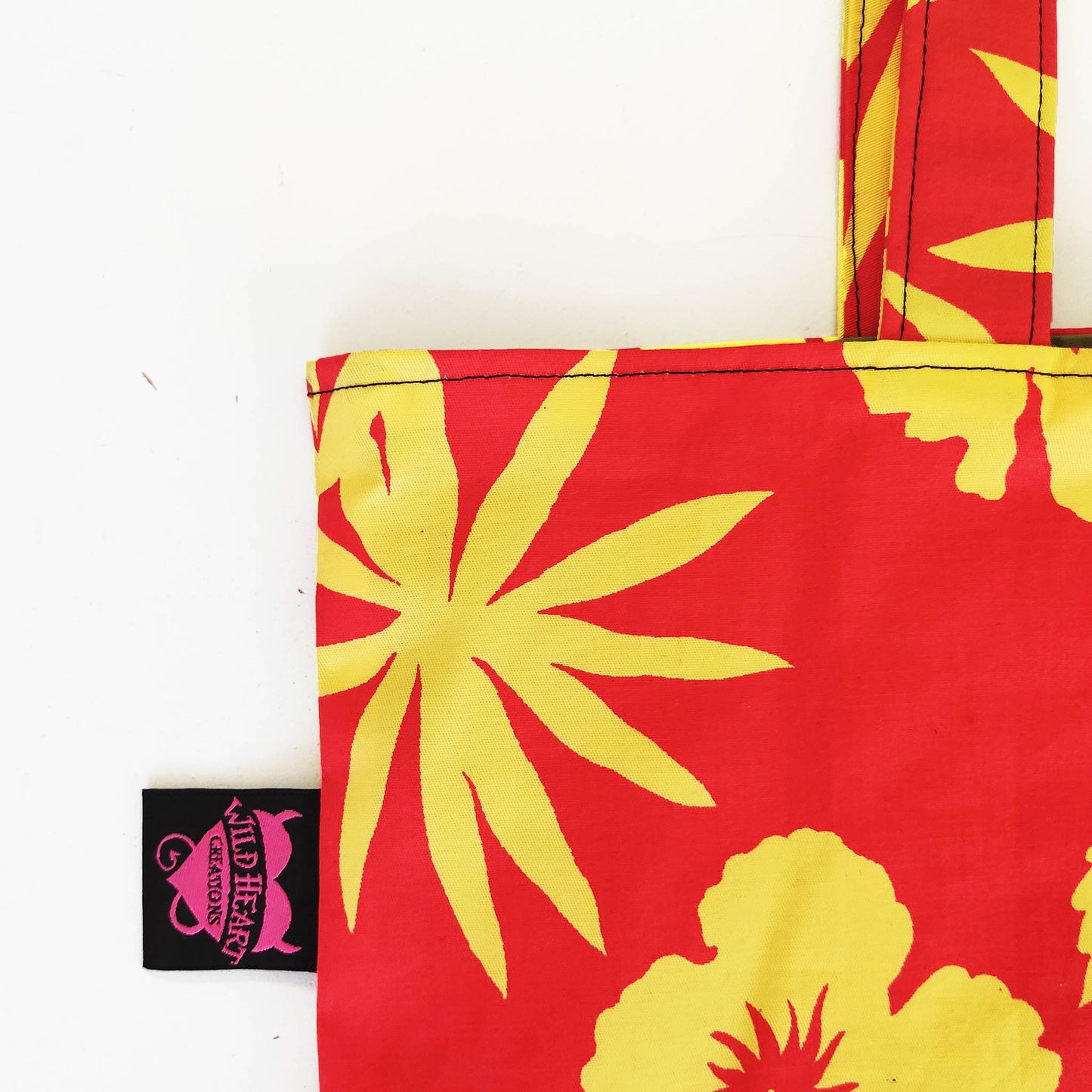 Die handgefertigte Tote Tasche hat ein lebendiges Hibiskusblüten-Motiv welches sich über die gesamte Oberfläche der Tasche erstreckt. Die leuchtenden Gelb- und Orangetöne erzeugen einen strahlenden Kontrast und verleihen der Tasche eine fröhliche und sommerliche Ausstrahlung. 