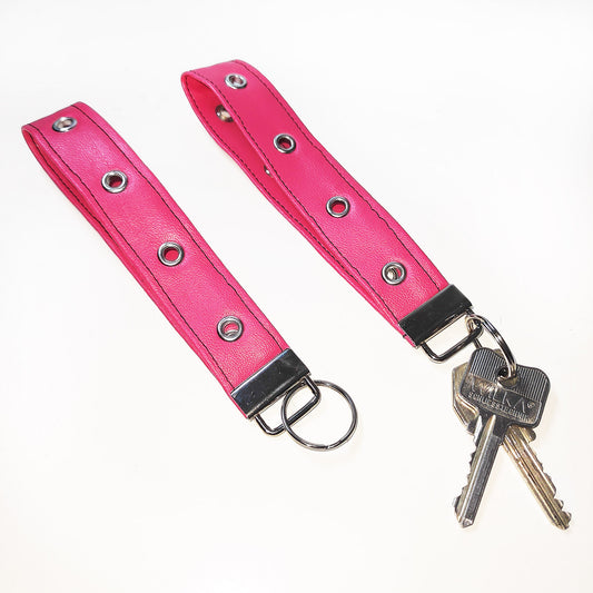 Handgemachter Schlüsselanhänger aus pinkem Lederimitat mit Ösen. Dieser praktische Anhänger kann bequem um das Handgelenk getragen werden, sodass er jederzeit griffbereit ist.
