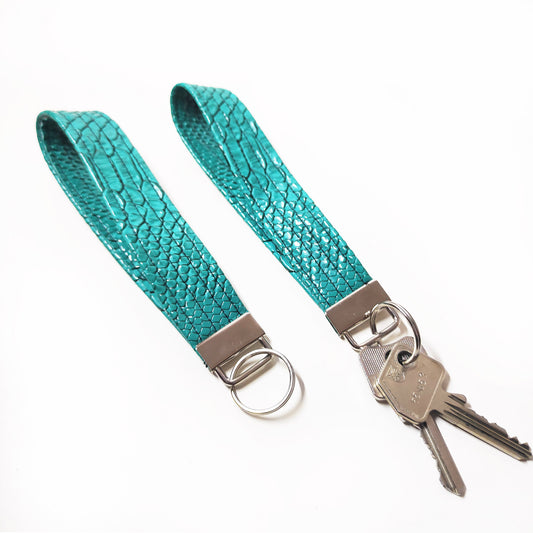 Handgemachter Schlüsselanhänger der aus türkisfarbenem Lederimitat mit Krokodil Optik gefertigt ist. Dieser praktische Anhänger kann bequem um das Handgelenk getragen werden, sodass er jederzeit griffbereit ist.