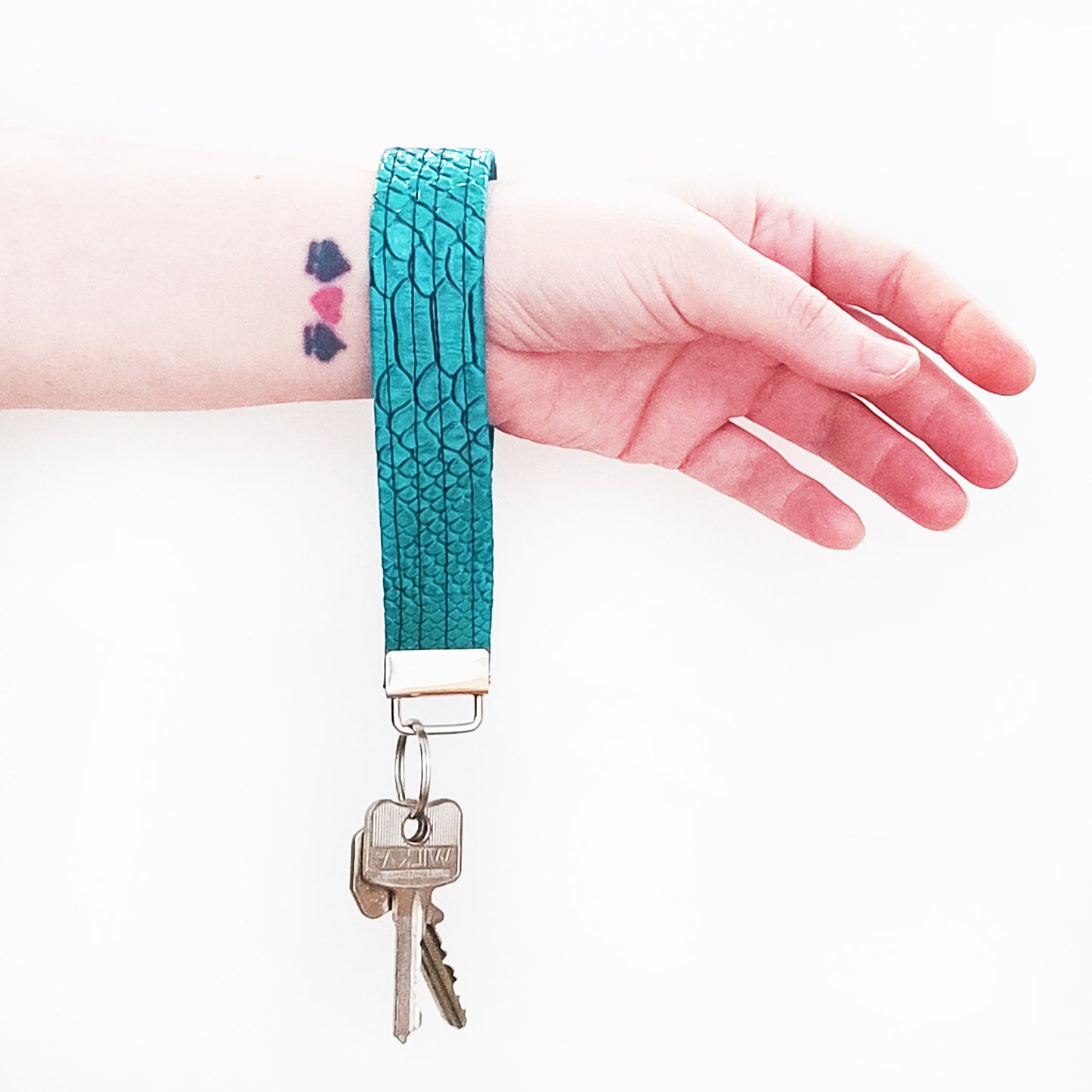 Handgemachter Schlüsselanhänger der aus türkisfarbenem Lederimitat mit Krokodil Optik gefertigt ist. Dieser praktische Anhänger kann bequem um das Handgelenk getragen werden, sodass er jederzeit griffbereit ist.