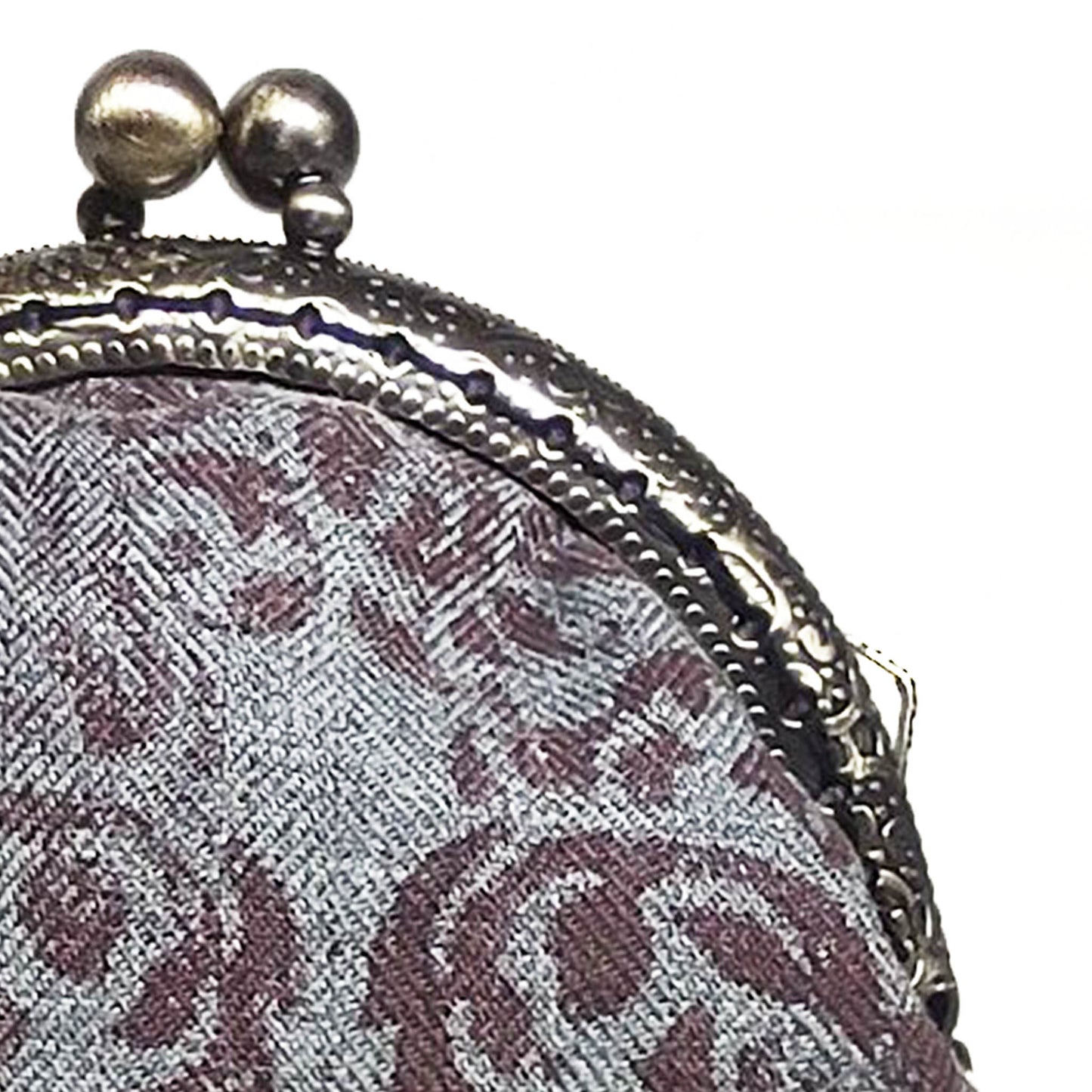 Diese Münztasche in grauem Fischgrat Stoff mit Ornamenten schließt mit einen bronzenen Kuss-Verschluss. Trotz ihrer kompakten Form bietet sie ausreichend Platz, um deine Münzen sicher aufzubewahren.